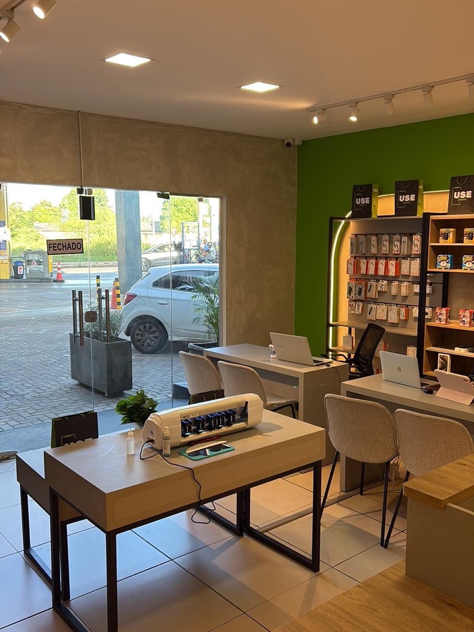 Salão da loja com mesas de atendimento, notebooks, máquina de película e parede verde